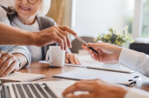 osoba starsza podpisująca umowę ubezpieczeniową przy stole